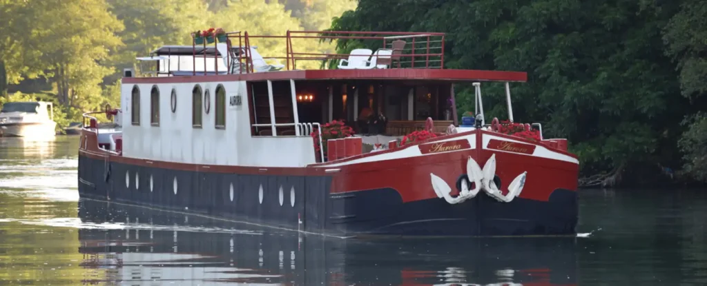 The hotel barge Aurora cruising a tree-lined canal